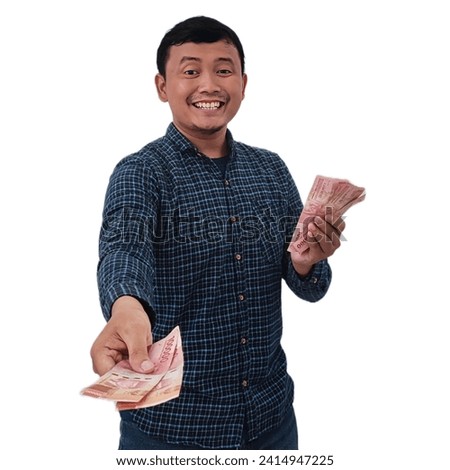 Smiling asian man holding money banknotes and pointing finger at camera, Expression of asian man holding money giving to you.  Asian man giving money for you. Man holding indonesian money rupiah.  Royalty-Free Stock Photo #2414947225