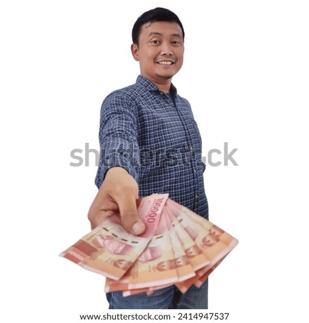 Smiling asian man holding money banknotes and pointing finger at camera, Expression of asian man holding money giving to you.  Asian man giving money for you. Man holding indonesian money rupiah.  Royalty-Free Stock Photo #2414947537