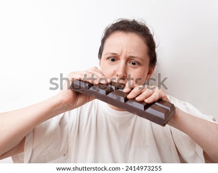Young woman with an effort breaks a large bar of dark chocolate with two hands on a white background




