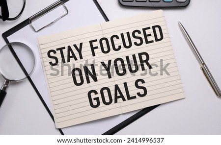 Inspirational quote - Stay focused on your goals. With text message on white paper book, pen, a cup of morning coffee, flower.