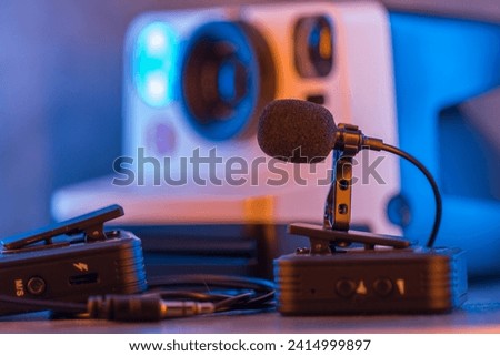 Close up on wireless lavalier microphones, an old fashioned camera is visible in the background, blurred.