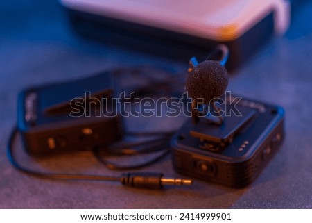 Close up on wireless lavalier microphones, an old fashioned camera is visible in the background, blurred.