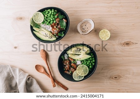 Buddha bowl with crispy sesame chicken asian style. Sweet and sour fried chicken with steamed rice, peas and acocado on light wooden background. Healthy and balanced food concept. Top view Royalty-Free Stock Photo #2415004171