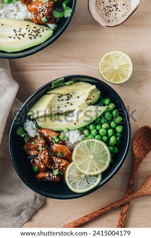 Buddha bowl with crispy sesame chicken asian style. Sweet and sour fried chicken with steamed rice, peas and acocado on light wooden background. Healthy and balanced food concept. Top view Royalty-Free Stock Photo #2415004179
