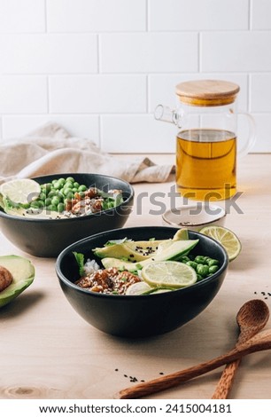 Buddha bowl with crispy sesame chicken asian style. Sweet and sour fried chicken with steamed rice, peas and acocado on light wooden background. Healthy and balanced food concept. Selective focus Royalty-Free Stock Photo #2415004181