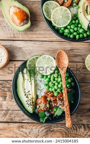 Buddha bowl with crispy sesame chicken asian style. Sweet and sour fried chicken with steamed rice, peas and acocado on rustic wooden background. Healthy and balanced food concept. Top view Royalty-Free Stock Photo #2415004185