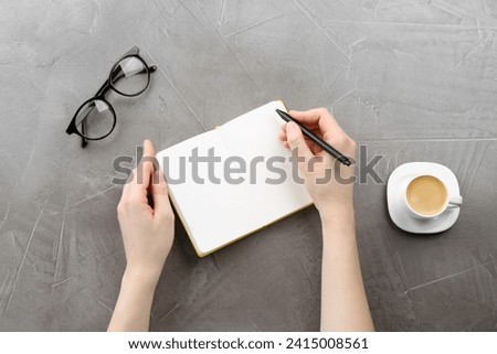 Woman writing in notebook at grey table, top view