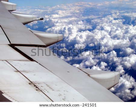 An airplane wing flying at high altitude above the clouds