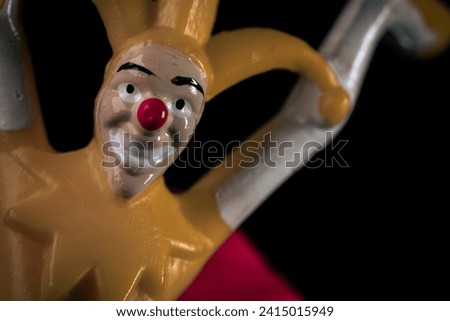 Weird face of a jester with a red nose on a black background. Dirty toy jester in the dark