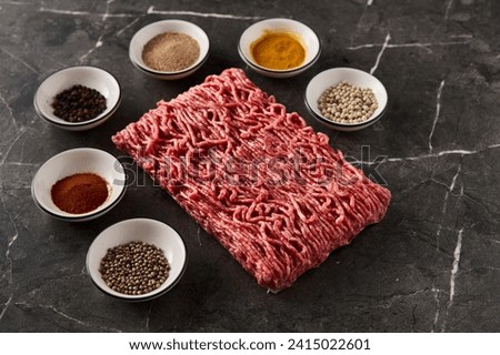 Raw and Fresh Minced Beef with spices for cooking on dark marble background. Minimalistic food photo, low-key.