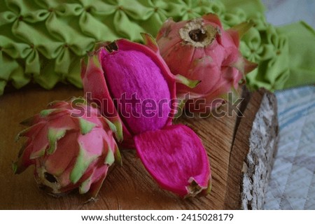 Ripe Red Meat Dragon Fruit with fallen peel showing the juicy meat of the fruit or Pink Pitaya with Whole Fruits in the Background on the rustic wooden board
