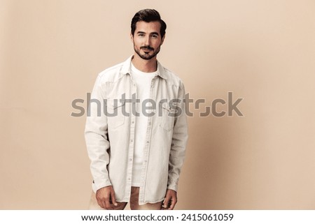 Stylish male smile model posing on a beige background in a white t-shirt looking at the camera, fashionable clothing style, copy space, space for text Royalty-Free Stock Photo #2415061059