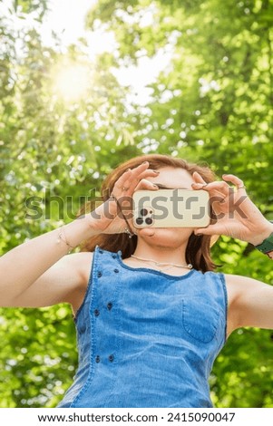 A woman takes a picture in nature with her smartphone. The smartphone covers her face.