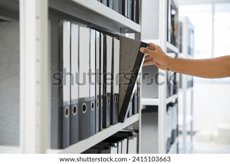 Hand of businessman office worker searching files and paperwork in the archive or document archiving storage room shelf for folder binder finding or data report record or workplace photo concept.