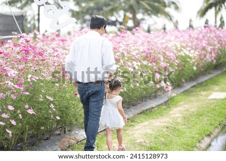 Little girl with her father on nature background A back view of the Father in Heaven concept. Father holds daughter's hand as she walks.