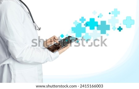 Doctor in a white coat on a light background with a tablet in his hands, blue and blue crosses. Medical Photography with Infographic, Crosses Flying Out of Tablet, Treatment and Health Care Concept