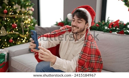 Young hispanic man celebrating christmas making selfie picture by smartphone at home