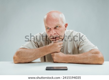 Man gripping chin, eyes locked on smartphone, visibly upset by disappointing digital experience Royalty-Free Stock Photo #2415194035