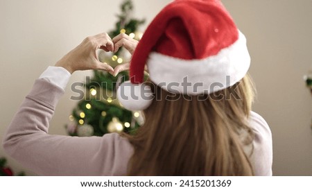 Young beautiful hispanic woman doing heart gesture standing by christmas tree at home