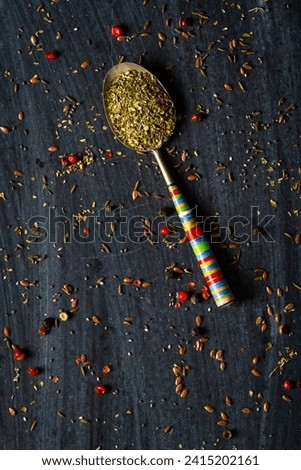 Old metal spoons with oregano on black background. Flat lay. Top view. Food concept. Dark mood food photography.