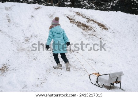 A little girl, a child climbs a mountain with a sled, going down the hill in the snow in winter. Photography, portrait, childhood concept, lifestyle.