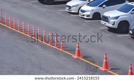 Row of cars parked on parking lots area with orange traffic cones and bollards demarcate traffic lane on the middle of asphalt street in outdoors car park area, high angle view