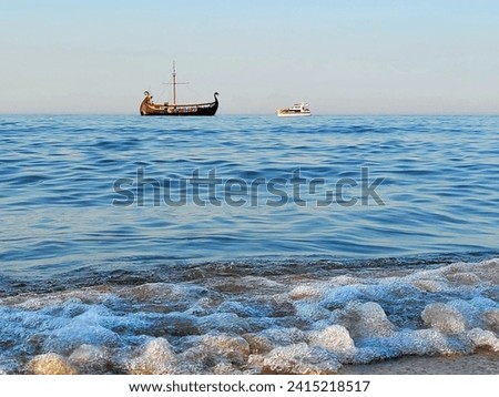 Two sea vessels met in the blue sea - a ship from the Viking era and a modern yacht. The waves hit the stones, the calm, beautiful cloudless sky. Beautiful picture