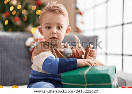 Adorable toddler unpacking christmas gift sitting on sofa at home