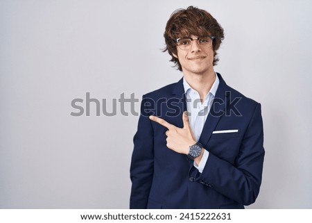Hispanic business young man wearing glasses cheerful with a smile on face pointing with hand and finger up to the side with happy and natural expression 