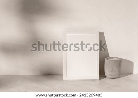 Empty white picture frame mockup with copy space, candle on marble table background, textured neutral warm white plaster wall with soft sunlight shadows, minimal home interior poster template.