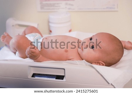 Cute little baby newborn lying in diaper on scale to measure weight during childbirth