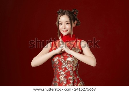 Beautiful young Asian woman with clean fresh skin wearing traditional cheongsam qipao dress posing on red background. Portrait of female model in studio. Happy Chinese new year. Royalty-Free Stock Photo #2415275669