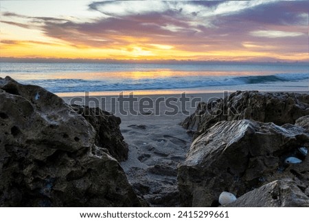 Radiant sunrise over a serene beach, framed by rugged rocks, perfect for invigorating morning themes, travel blogs, and creative designs.