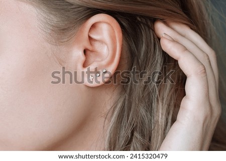 Ear piercing. Cropped shot of a young woman wearing three stud earrings on the earlobe. Jewelry with gemstones, accessories, a cross with fianits Royalty-Free Stock Photo #2415320479
