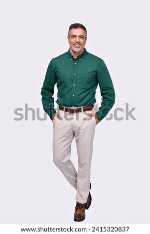 Confident elegant middle aged business man entrepreneur, smiling older professional stylish businessman wearing green shirt looking at camera standing isolated on gray, full length vertical portrait.