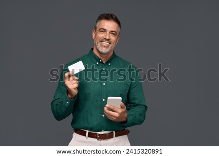 Happy middle aged business man, smiling mature businessman holding mobile phone and credit debit card mockup using banking finance app making online purchase on smartphone isolated on gray background. Royalty-Free Stock Photo #2415320891