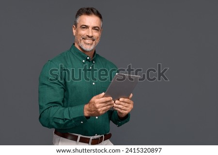 Smiling mature businessman professional executive manager looking at camera holding tab device, portrait. Happy middle aged business man ceo standing isolated on gray using digital tablet.