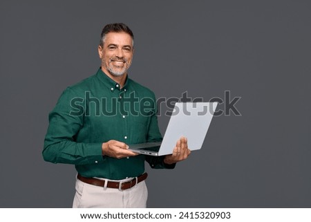 Happy middle aged business man ceo wearing green shirt standing isolated on gray using laptop. Smiling mature businessman professional executive manager looking at camera holding computer. Portrait