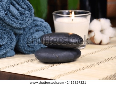 Spa massage hot stones, towels and candle on wooden background still life stock photo images. Spa and wellness setting with towels, candle and pebbles on bamboo mat. Beauty spa treatment composition