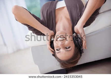 Happy woman, upside down on couch and headphones for music, audio streaming and wellness with fun at home. Podcast, radio playlist and subscription online, relax in living room with technology