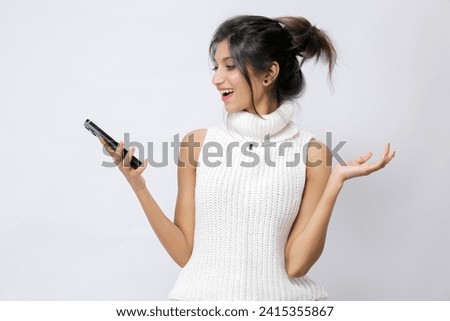 Photo of Young and beautiful Pakistani millennial lady look using phone knitted white sleeveless sweater with turtle neck isolated on white background