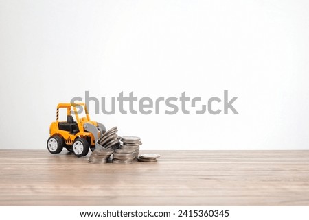 A yellow-colored bulldozer is scooping the pile of coins on the wooden table on a white background. Business and finance concept.