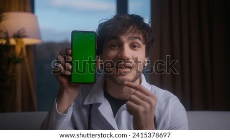 Young male doctor wear uniform with stethoscope show app on the phone screen. Doctor demonstrating smartphone with green screen chroma key. Concept of programs and advertising for medicine
