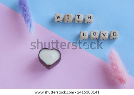 Caption with love next to flowers and heart shaped dark and white chocolate candy in dark and white chocolate. Pink and blue gendered background for valentine's day. Photo. Close-up