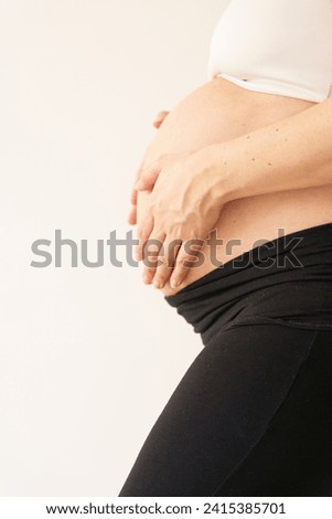 Side View of a Pregnant Woman. A beautiful composition capturing the side profile of a pregnant woman adorned in a white top, showcasing her bare abdomen and legs clad in black leggings Royalty-Free Stock Photo #2415385701