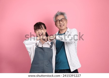 Asian senior man and woman couple in overalls casual clothing with gesture of cheerful, excited and celebrating isolated on pink background. St Valentine's Day, Women's Day, Birthday