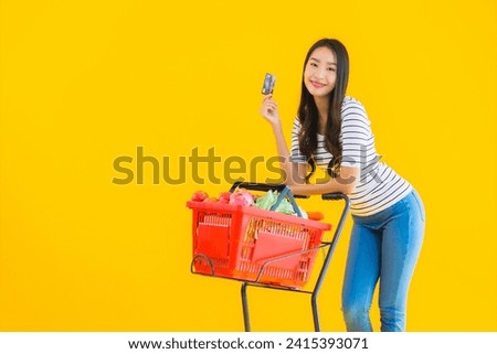 Portrait beautiful young asian woman shopping grocery cart from supermarket with credit card on yellow isolated background