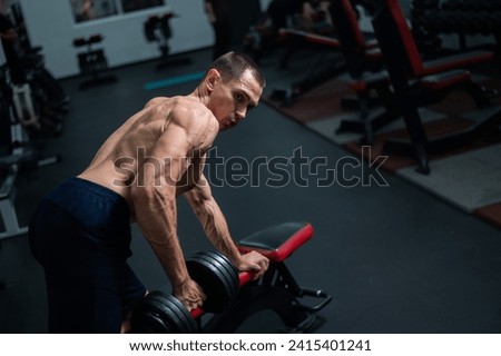 Shirtless man doing dumbbell row to waist on bench at gym.  Royalty-Free Stock Photo #2415401241