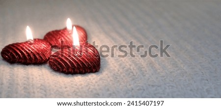 Three burning red candles in the shape of hearts lie on a light knitted surface. The concept of Valentine's Day, romance, warmth and homeliness. Advertising banner with copy space