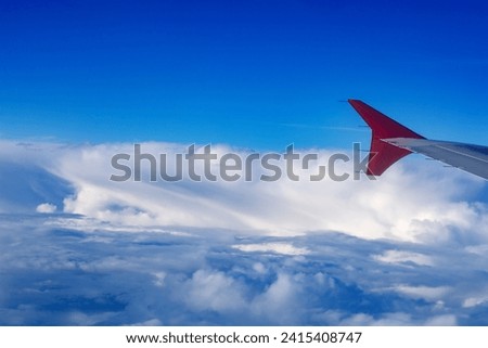 A part of an airplane wing with a red tip in flight above the clouds